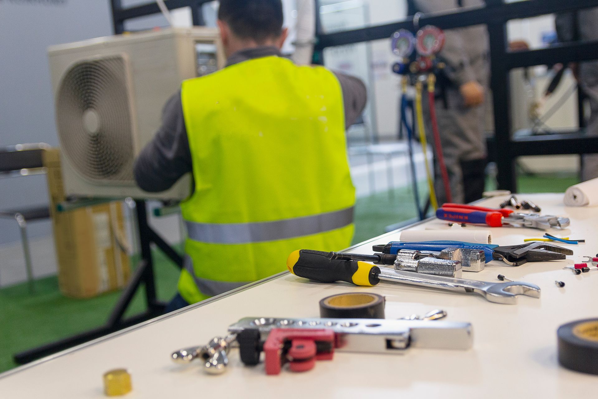 Tools on a workbench with a technician servicing an HVAC unit in the background.