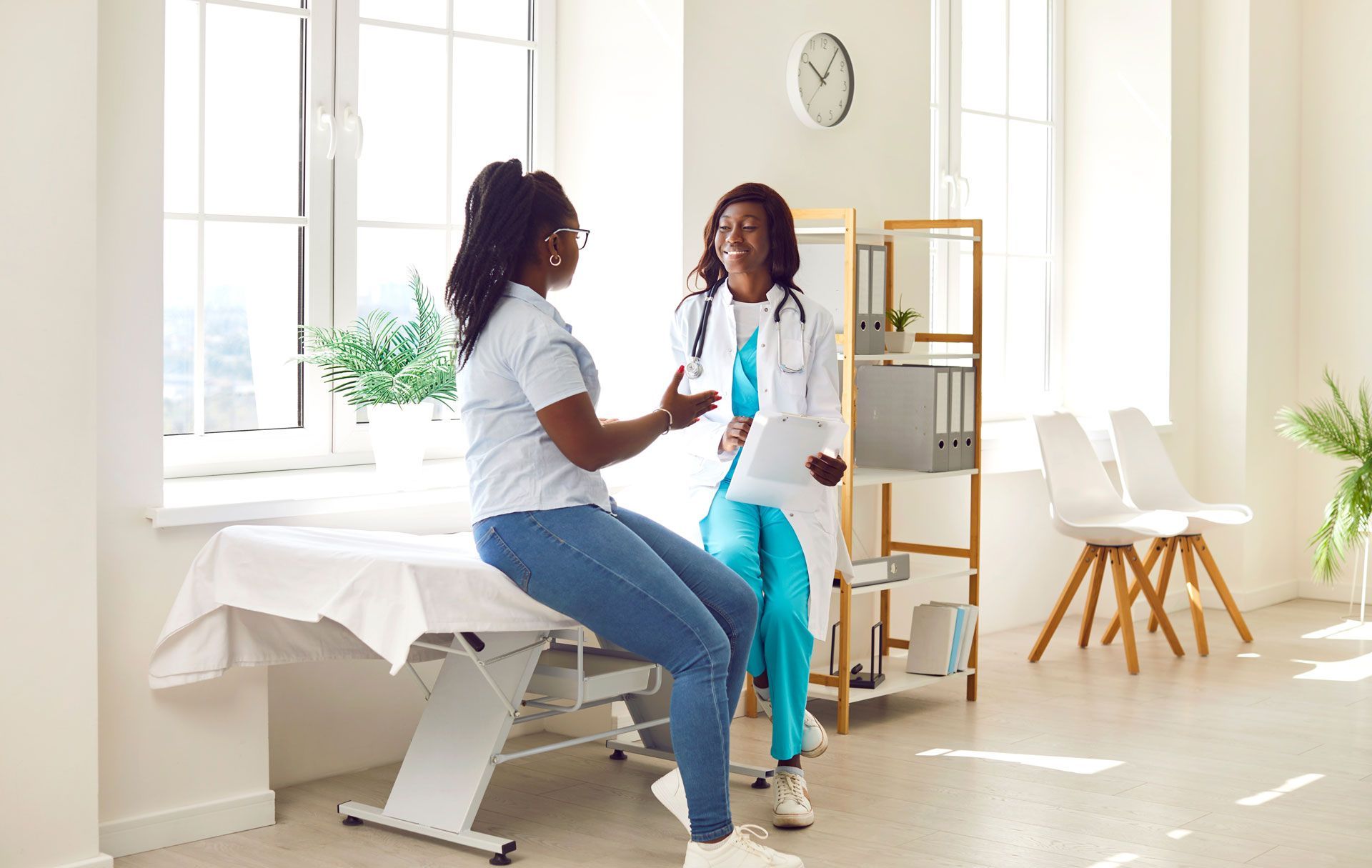 Doctor and patient in an exam room; the patient sits on the exam table while the doctor stands, gesturing.