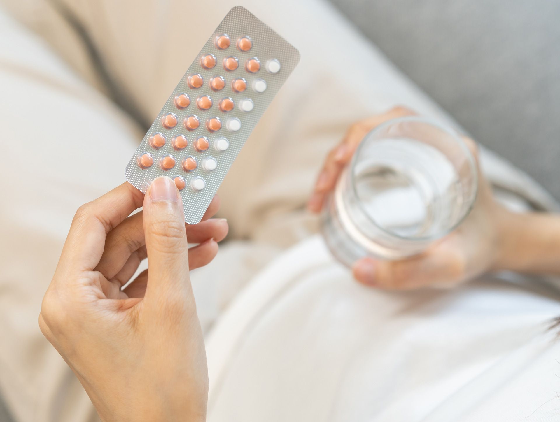 Person holding birth control pills and a glass of water.