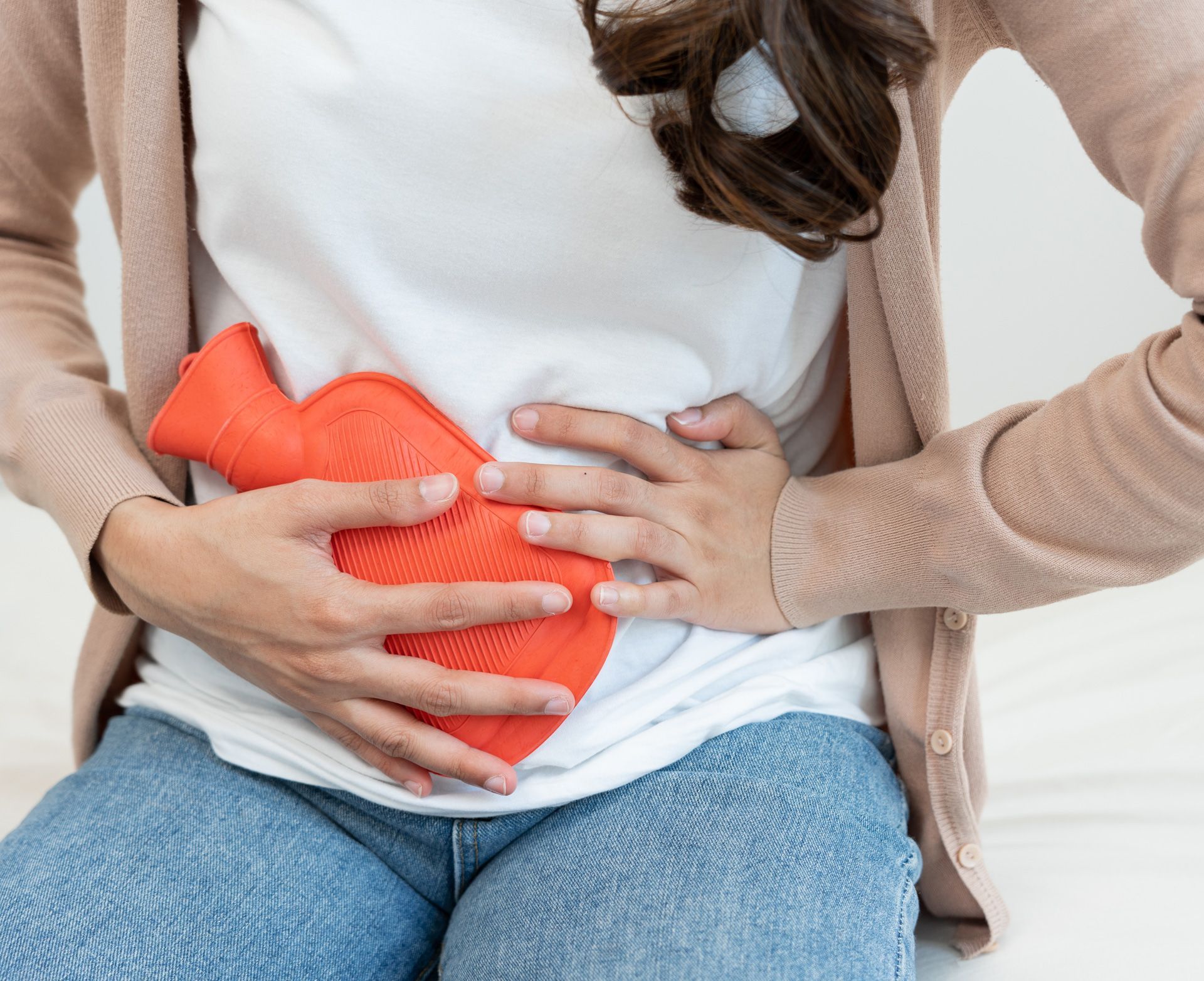 Woman holds hot water bottle on her abdomen, indicating possible menstrual pain.