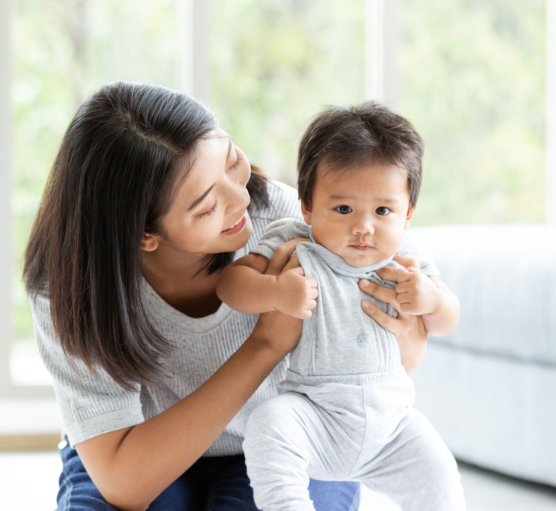 Woman holding a baby, helping it stand. Soft lighting, blurred background.