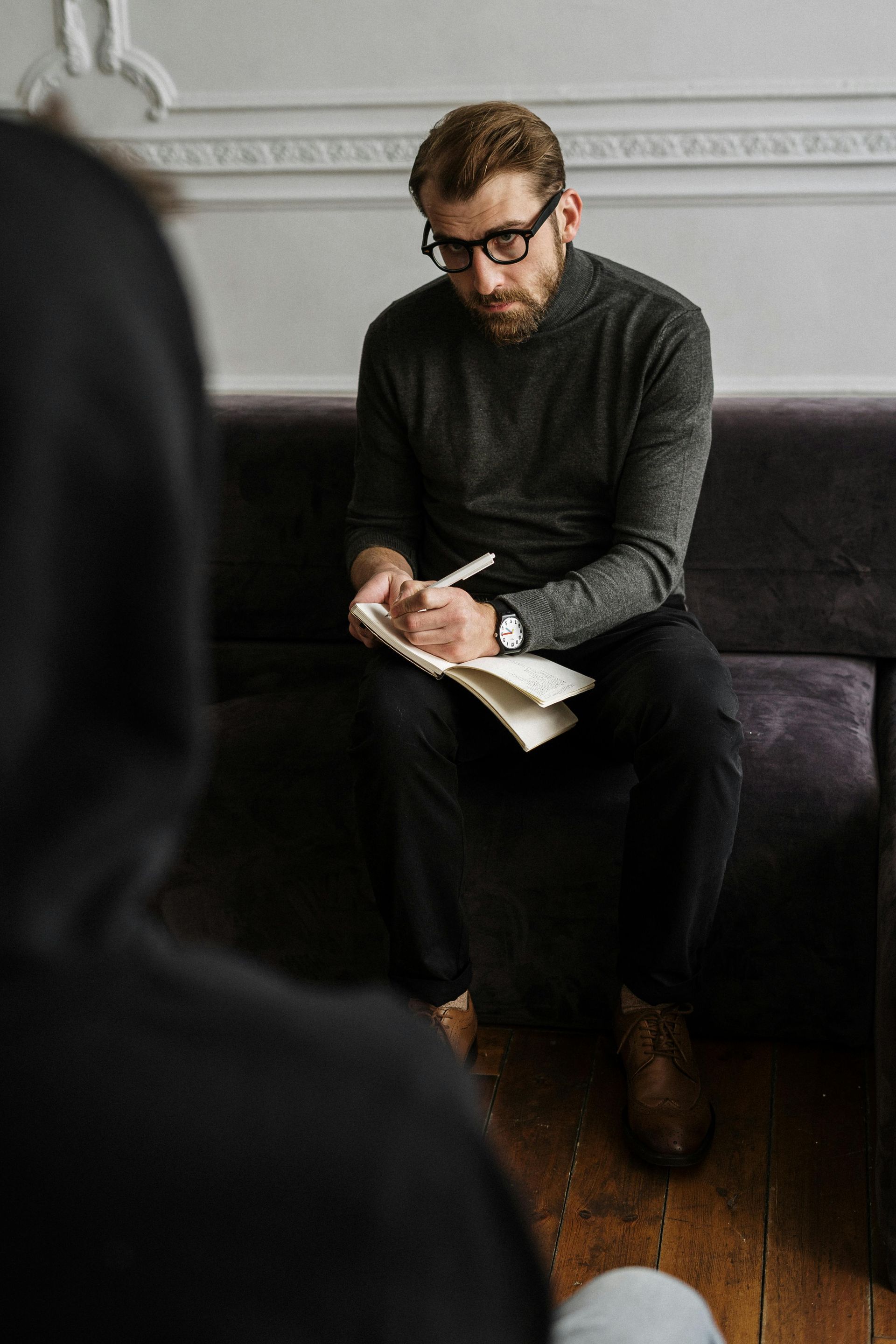 A man is sitting on a couch writing in a notebook.