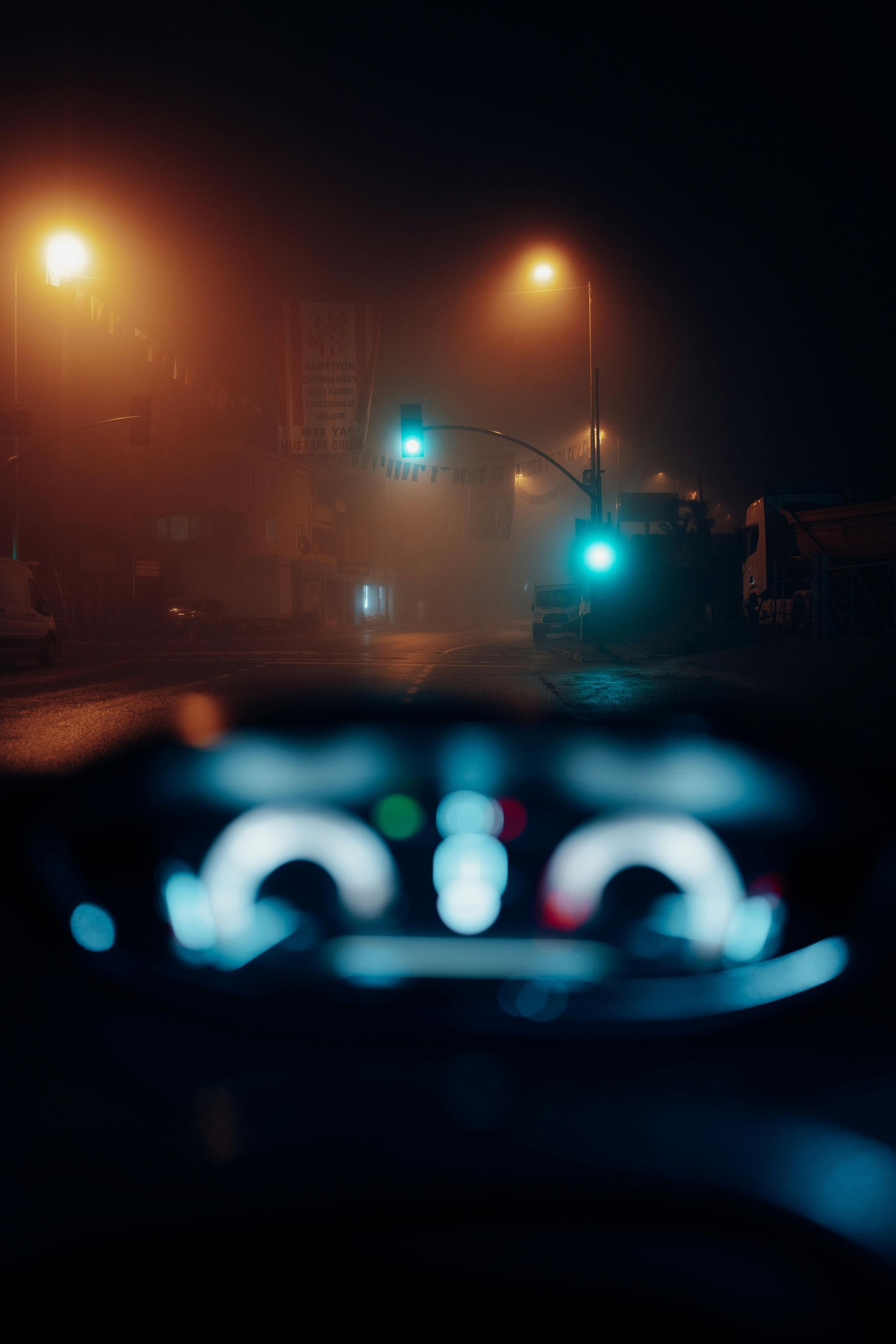 A car is driving down a foggy street at night.