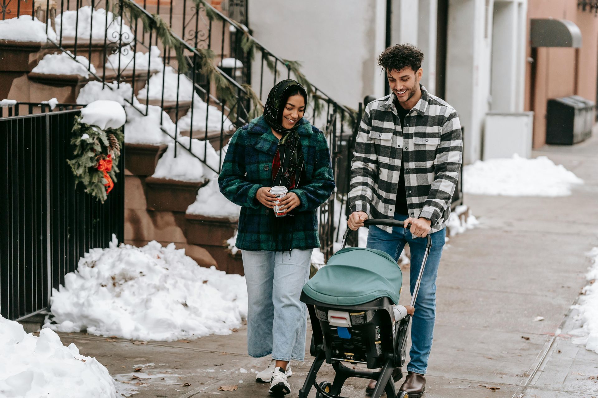 A man and woman are pushing a stroller down a snowy sidewalk.