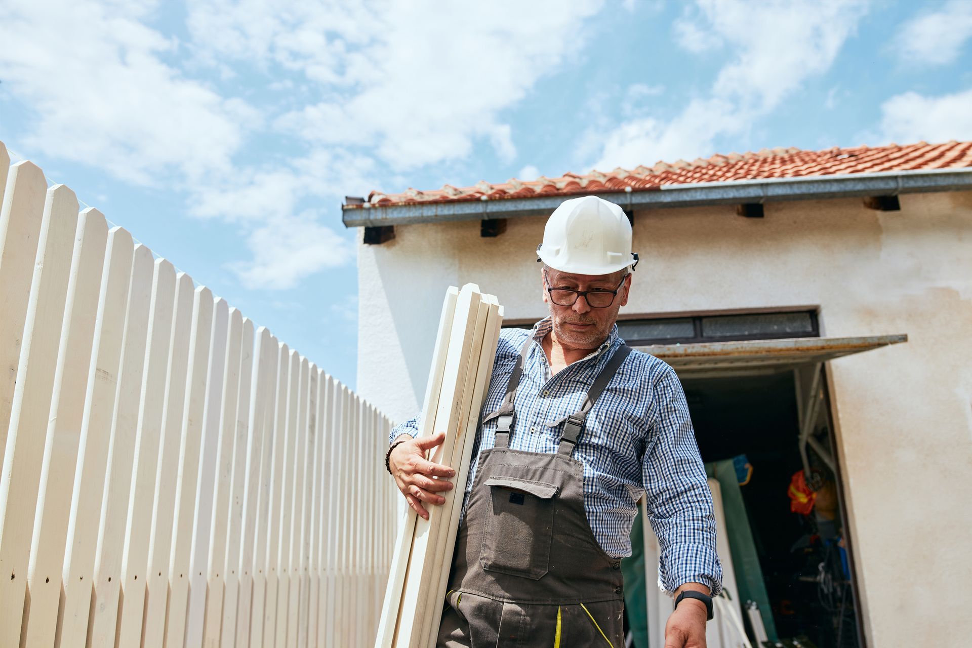 A man in a hard hat holds a wooden fence, showcasing his work in fence installation service.