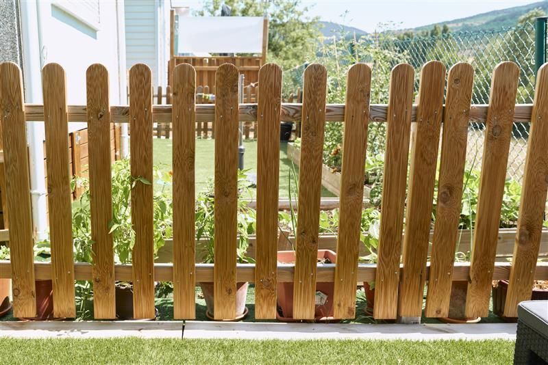Wooden picket fence in a backyard, with potted plants behind it and mountains in the distance.