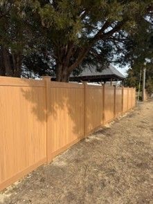 Wooden privacy fence along a dry roadside with trees overhead