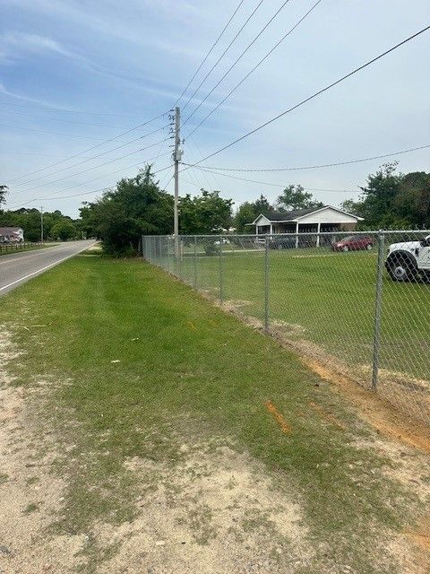 A chain link fence surrounds a grassy field next to a road.
