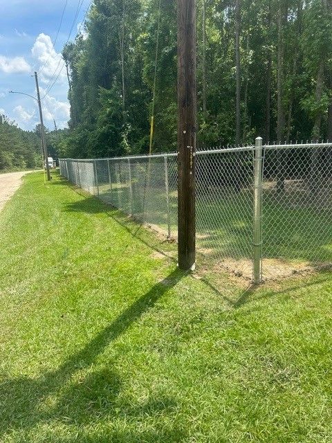 A chain link fence surrounds a grassy field next to a dirt road.