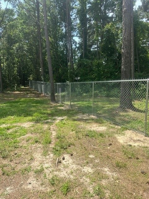 A chain link fence surrounds a grassy field in the middle of a forest.