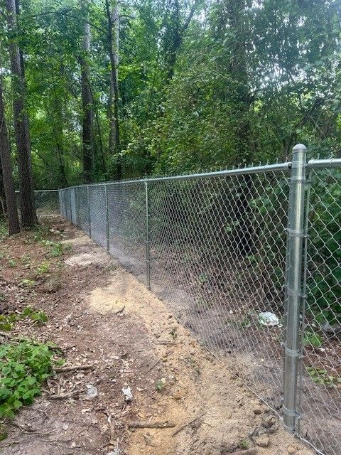 A chain link fence surrounds a dirt path in the woods.