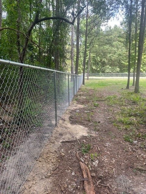 A chain link fence surrounds a dirt path in the middle of a forest.