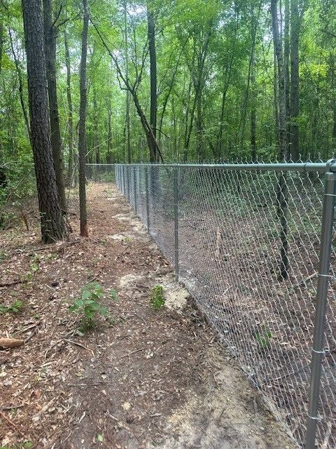 A chain link fence surrounds a path in the woods.