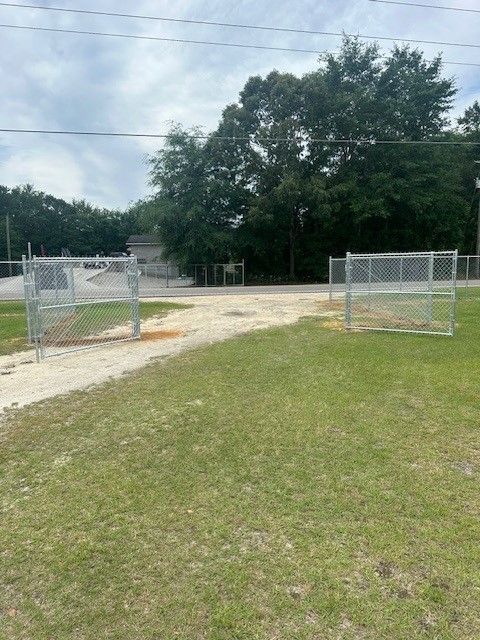 A chain link fence surrounds a grassy field with trees in the background.