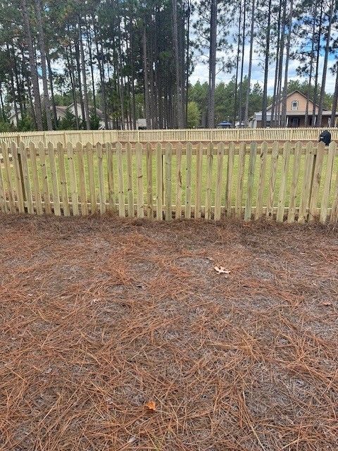 A wooden fence is surrounded by pine needles in a yard.