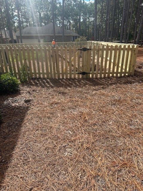 A wooden picket fence with a gate is in the backyard of a house.