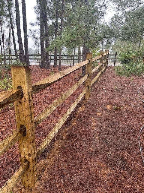 A wooden fence with a wire fence in the middle of a forest.