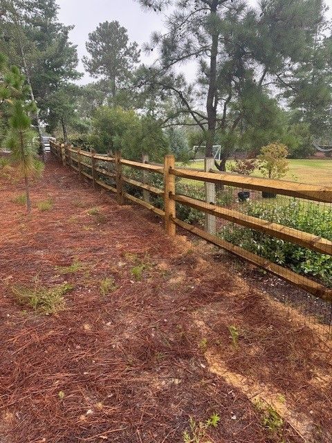 A wooden fence is surrounded by trees and pine needles.
