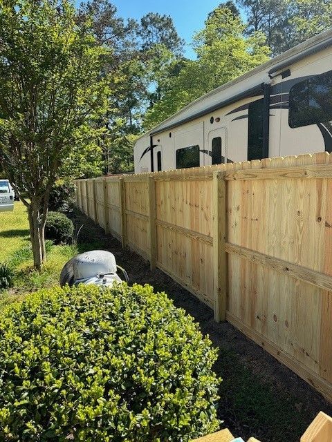 A wooden fence surrounds a house with a trailer in the background.