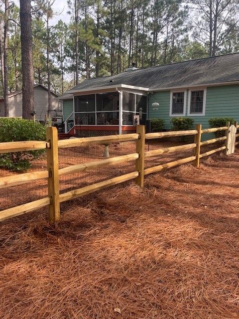A wooden fence is in front of a green house.