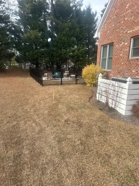 A backyard with a fence and a brick house in the background.