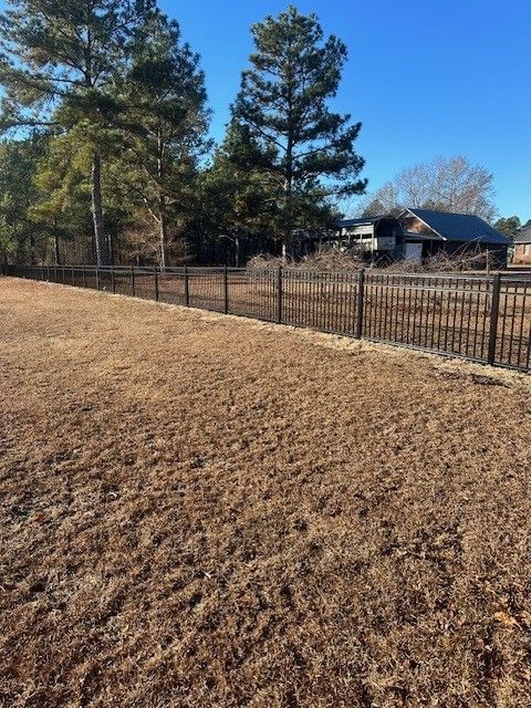 A fence surrounds a dry grass field with trees in the background