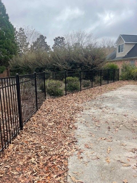 A fence with leaves on the ground in front of a house