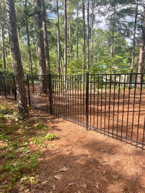 A metal fence is in the middle of a forest.