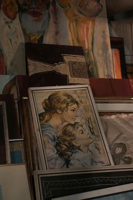 Artwork display: a painting of two women, one looking up, stacked with other framed art.