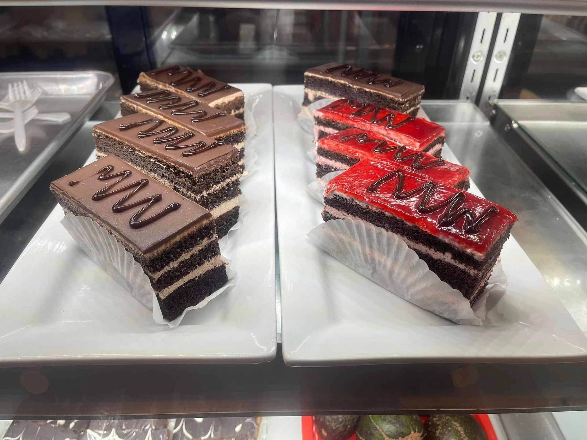 Assorted chocolate and red-glazed cake slices displayed in a bakery case