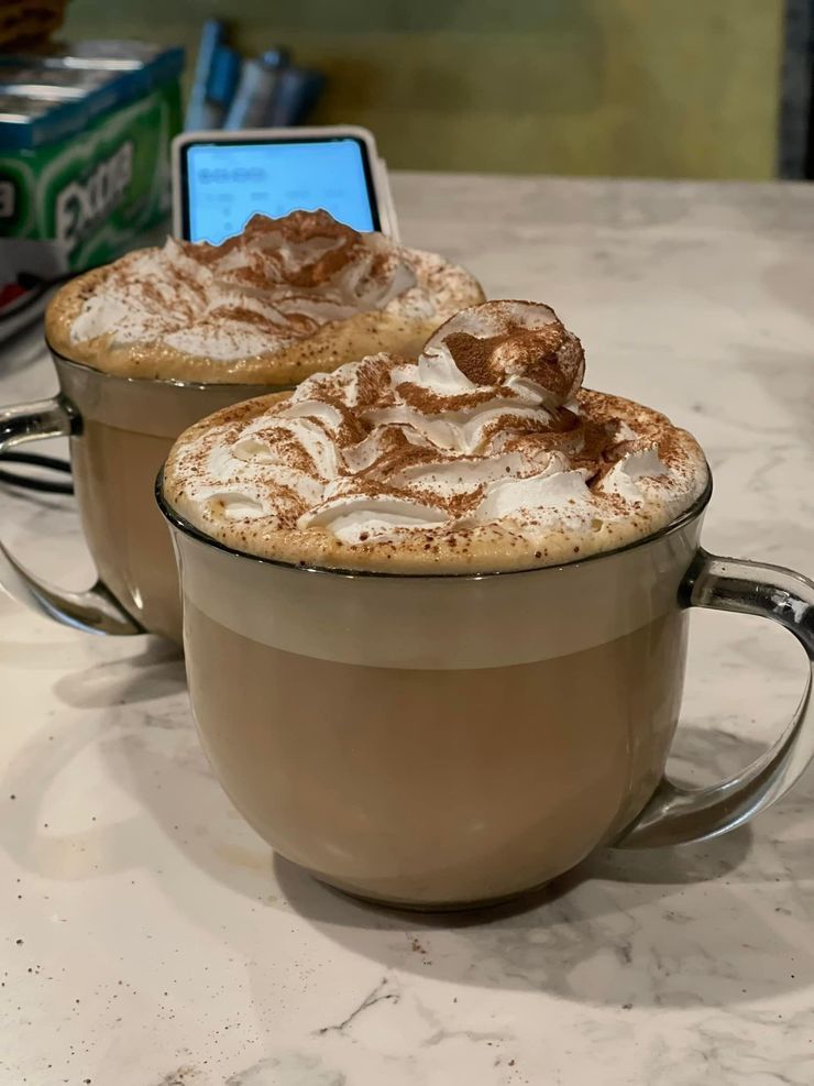 Two mugs of cappuccino topped with whipped cream and cinnamon on a café table