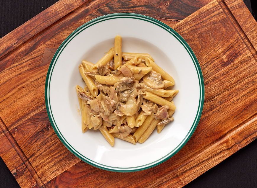 a bowl of pasta with mushrooms on a wooden cutting board