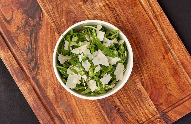 a bowl of salad with parmesan cheese on a wooden cutting board .