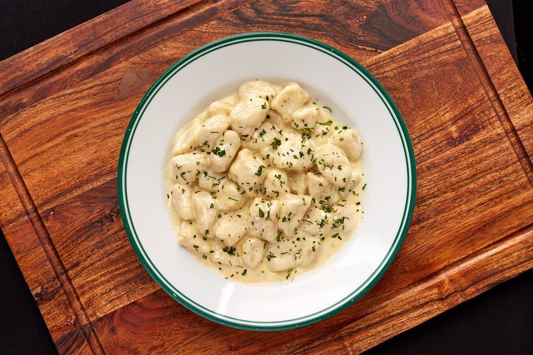 a bowl of gnocchi is on a wooden cutting board