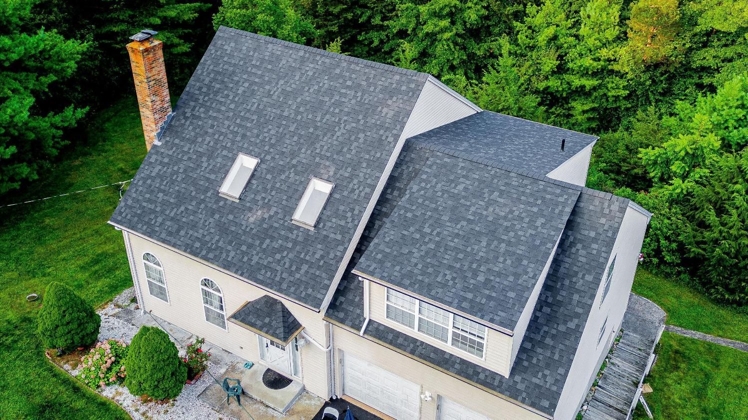 An aerial view of a house with a black roof with two skylights on the roof