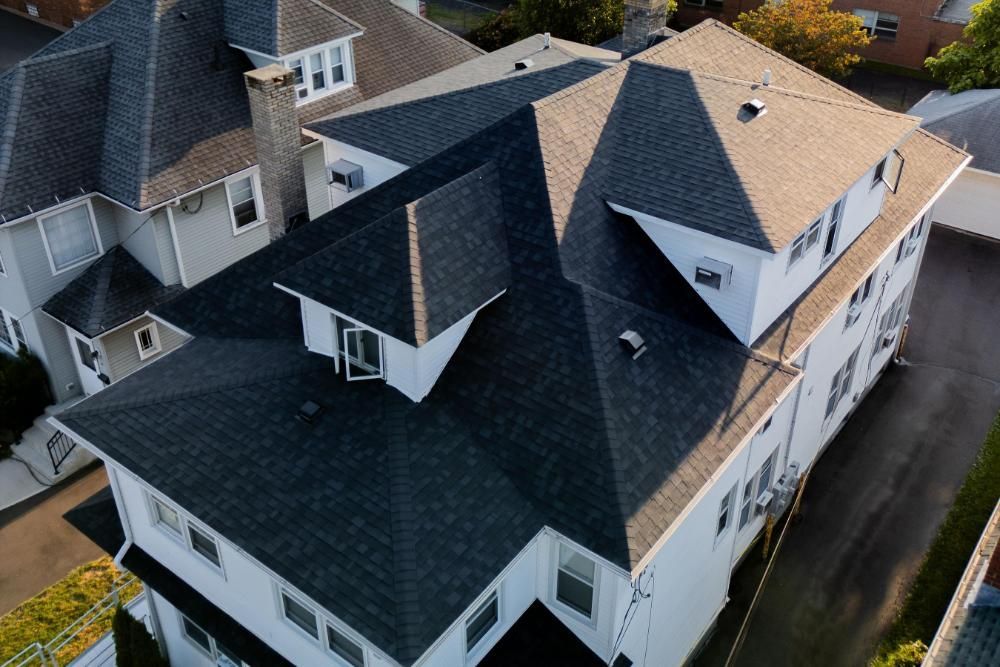 An aerial view of a large white house with a black asphalt roof.