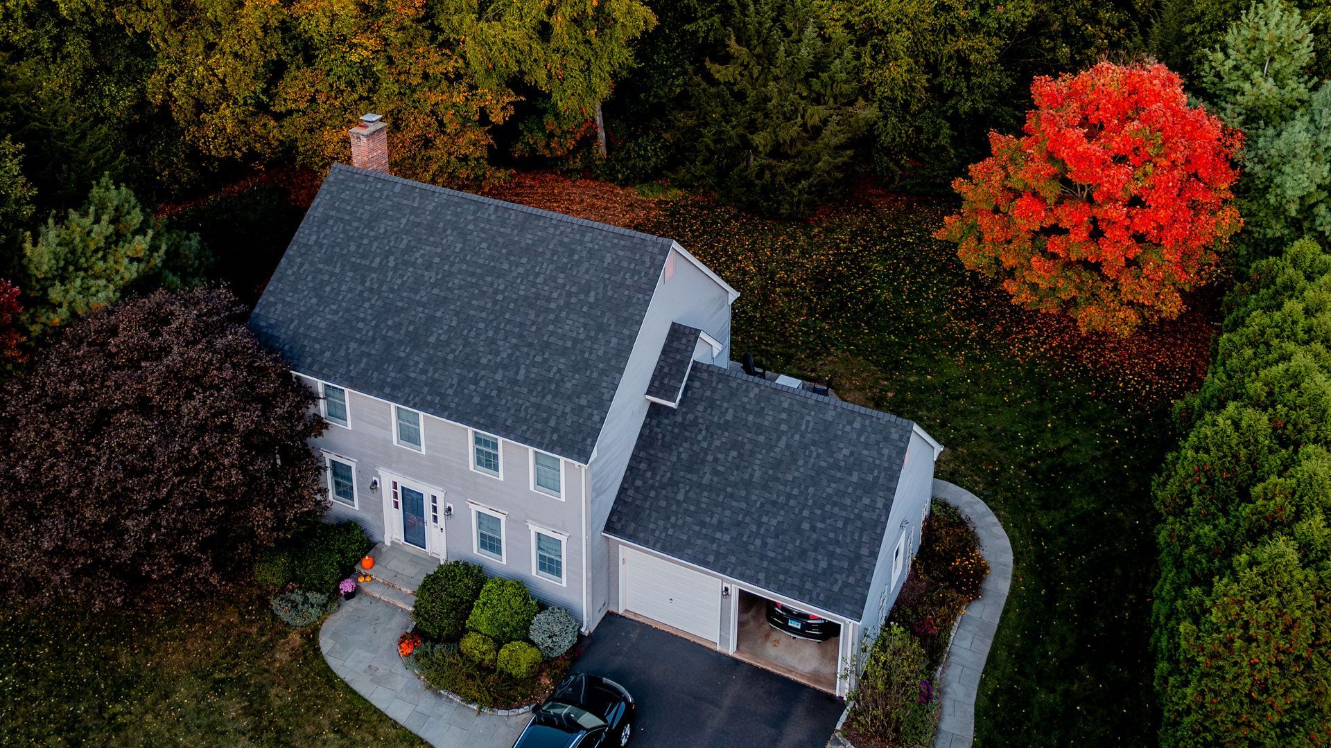 An aerial view of a house with a car parked in front of it surrounded by trees.