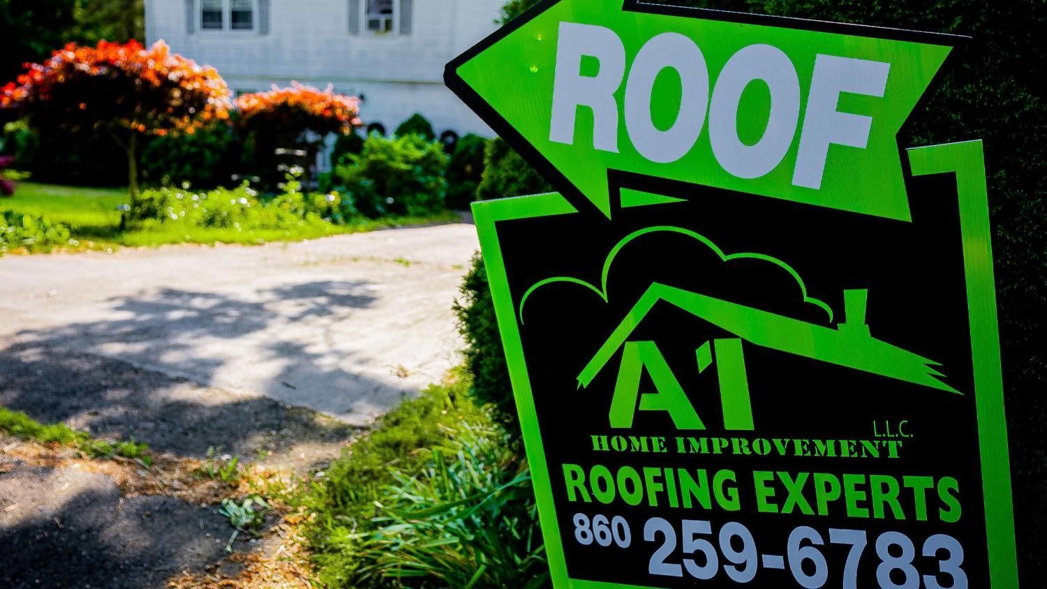 A sign for roofing experts is in front of a house