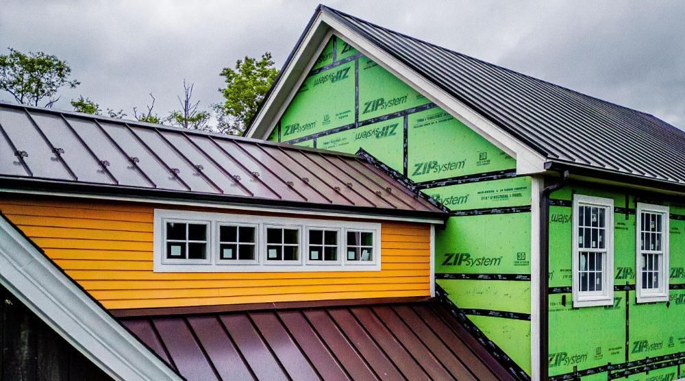 A house with a metal roof and green siding is being built.