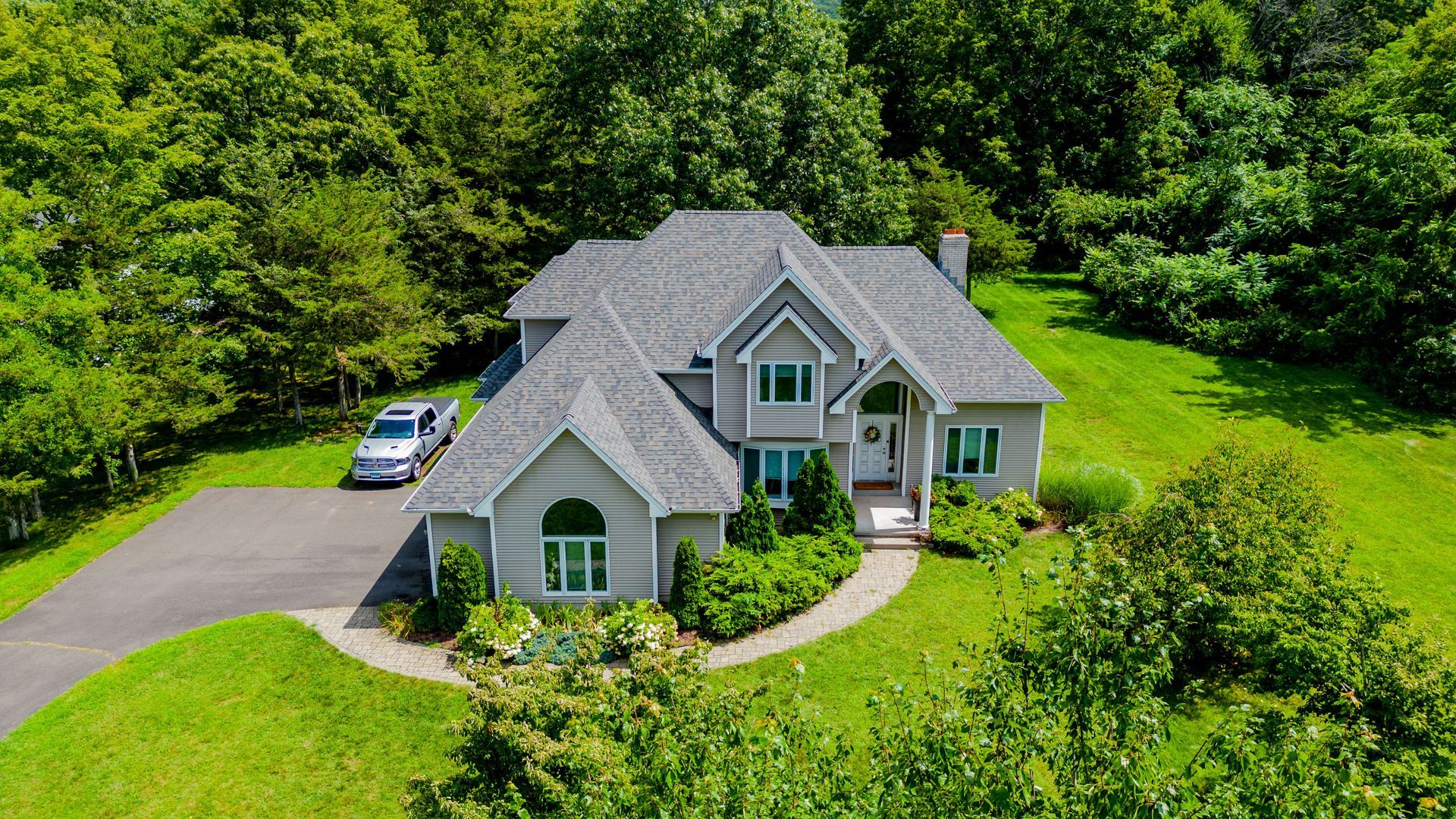 An aerial view of a large house with a car parked in front of it surrounded by trees.