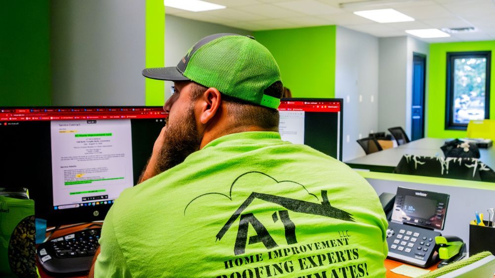 A man in a green shirt is sitting in front of a computer showing roofing warranties