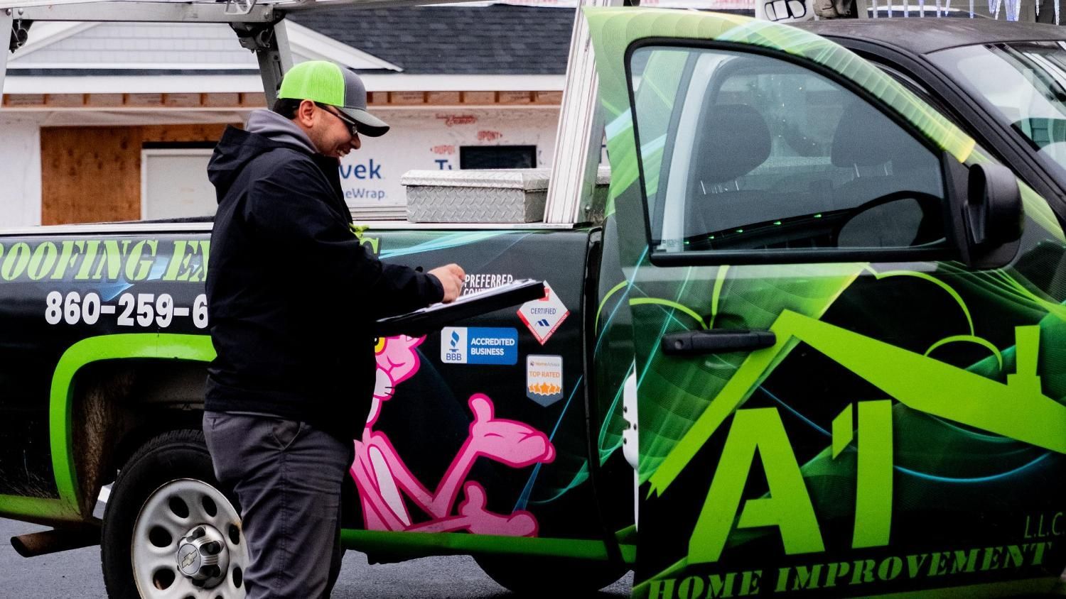 A man is standing next to a roofing company truck.