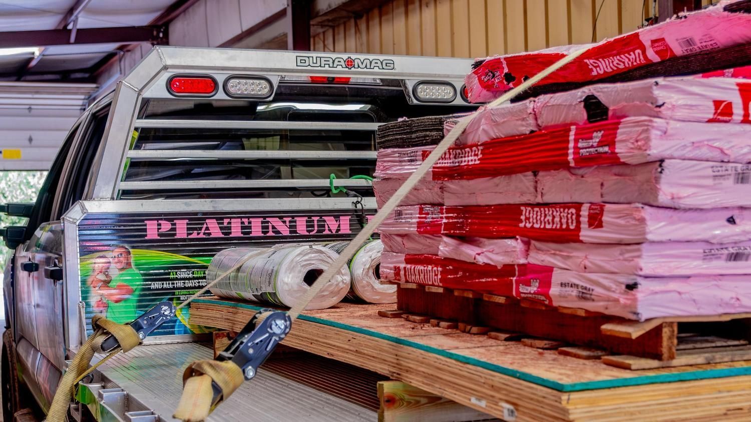 A truck is parked in a garage next to a stack of roofing materials