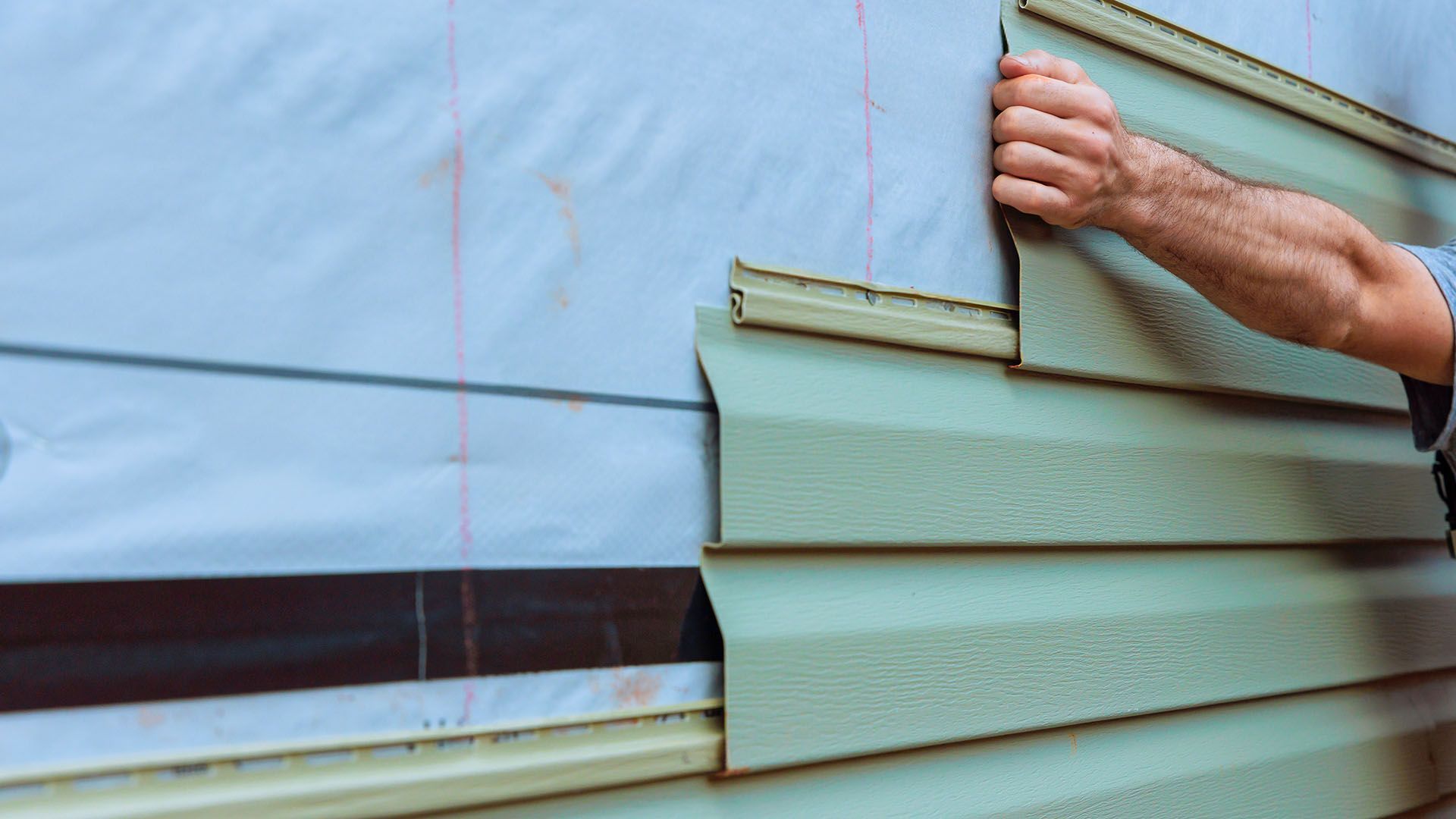 A man is installing siding on the side of a house.