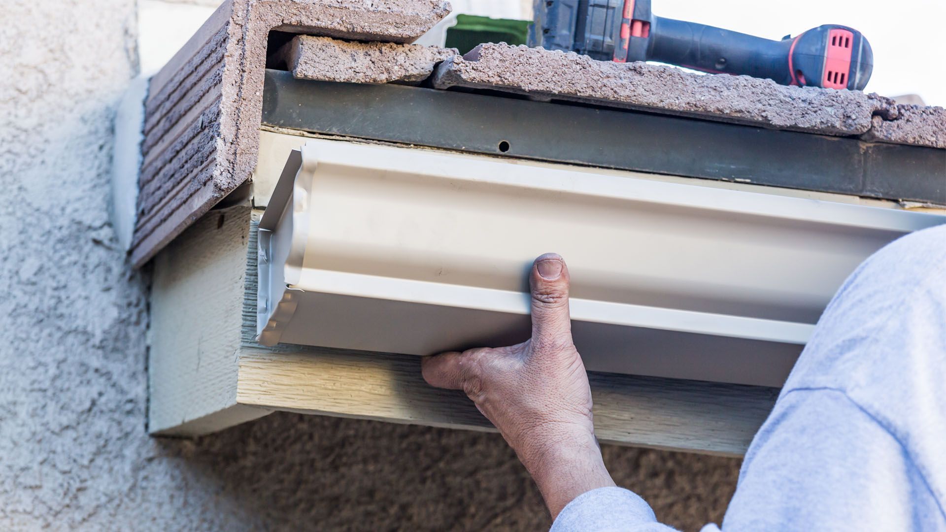 A man is installing a gutter on the side of a building.