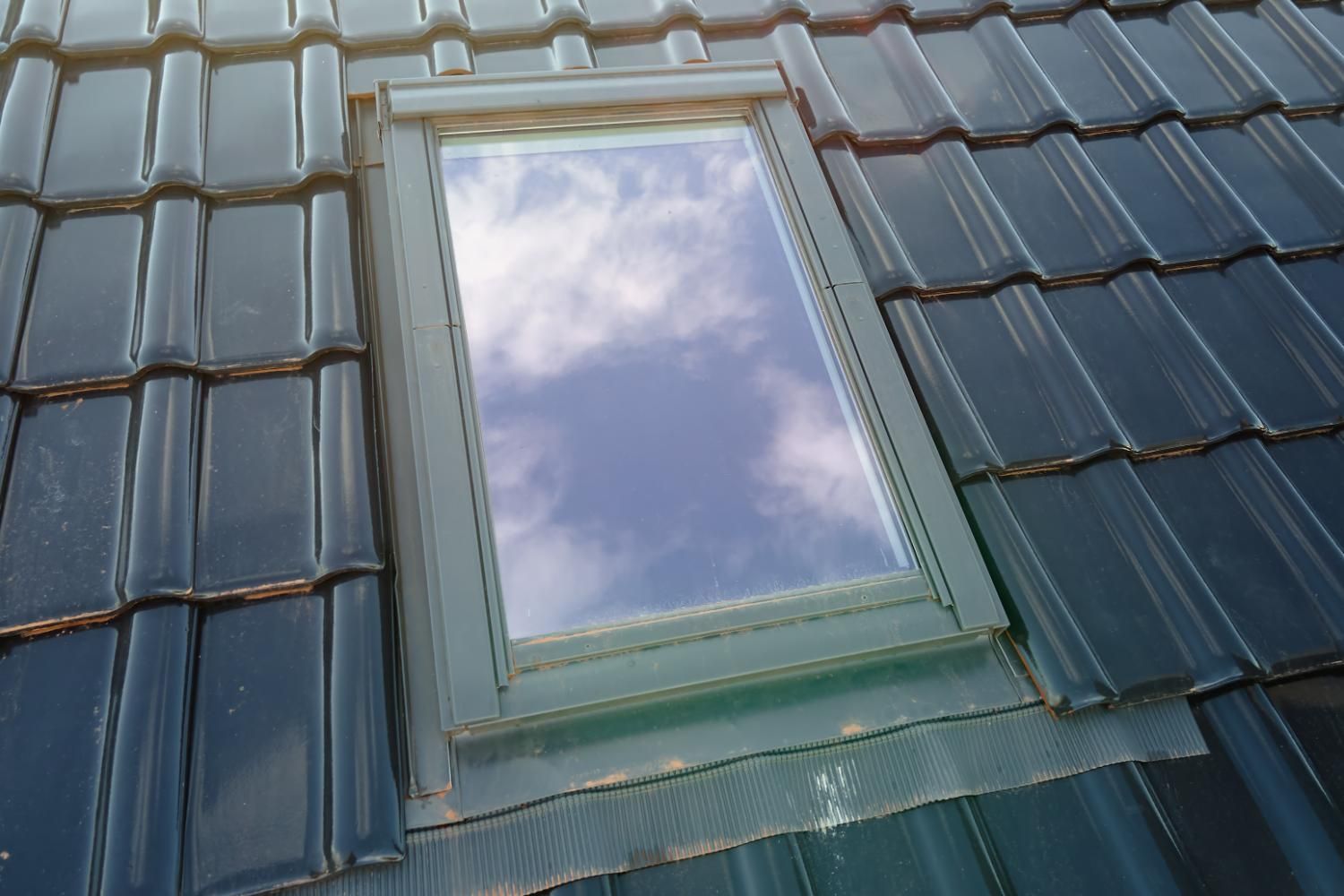 A window on the roof of a house with a cloudy sky reflected in it.