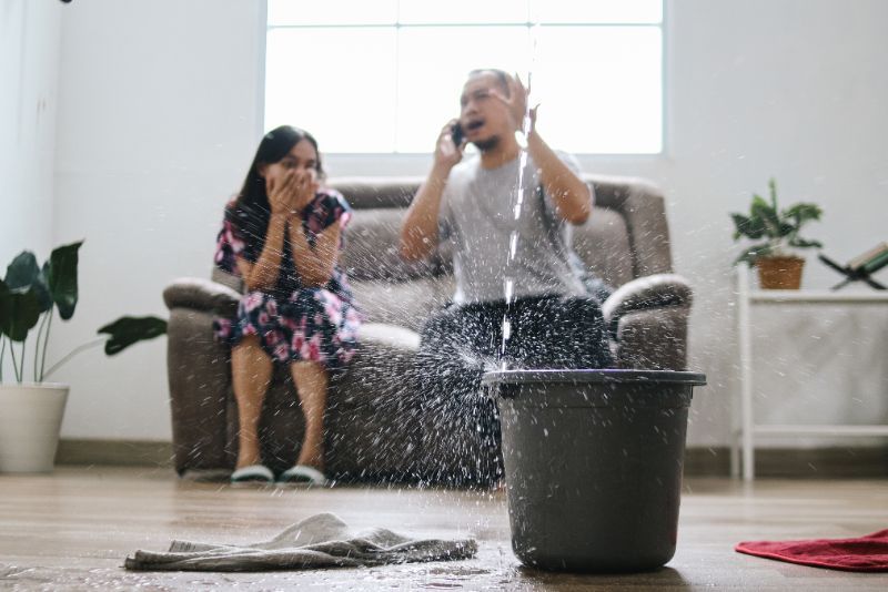 A man is sitting on a couch talking on a cell phone while a woman looks on.