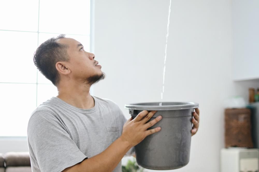 A man is holding a bucket collecting water from roof leak