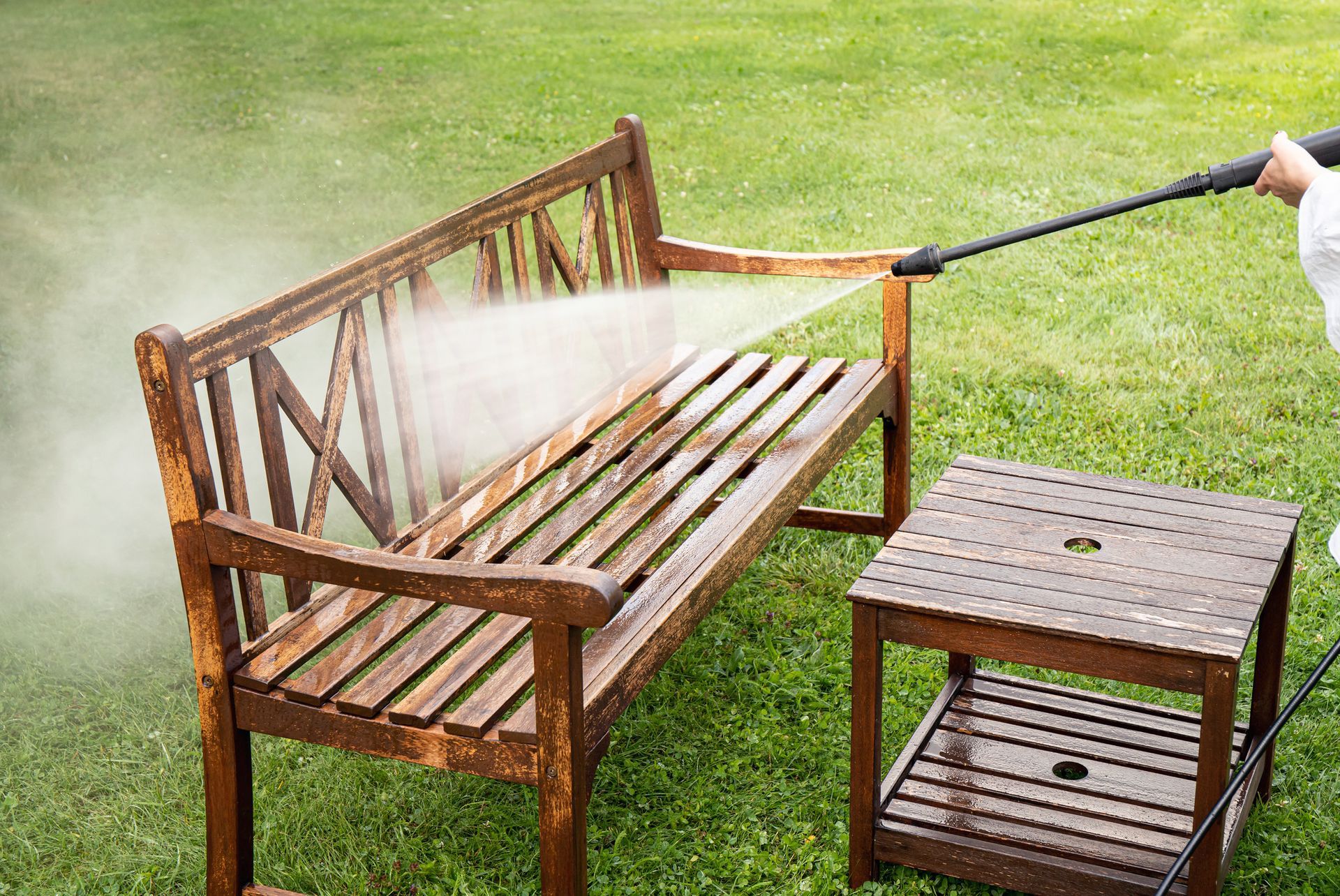 A person is cleaning a wooden bench with a high pressure washer.
