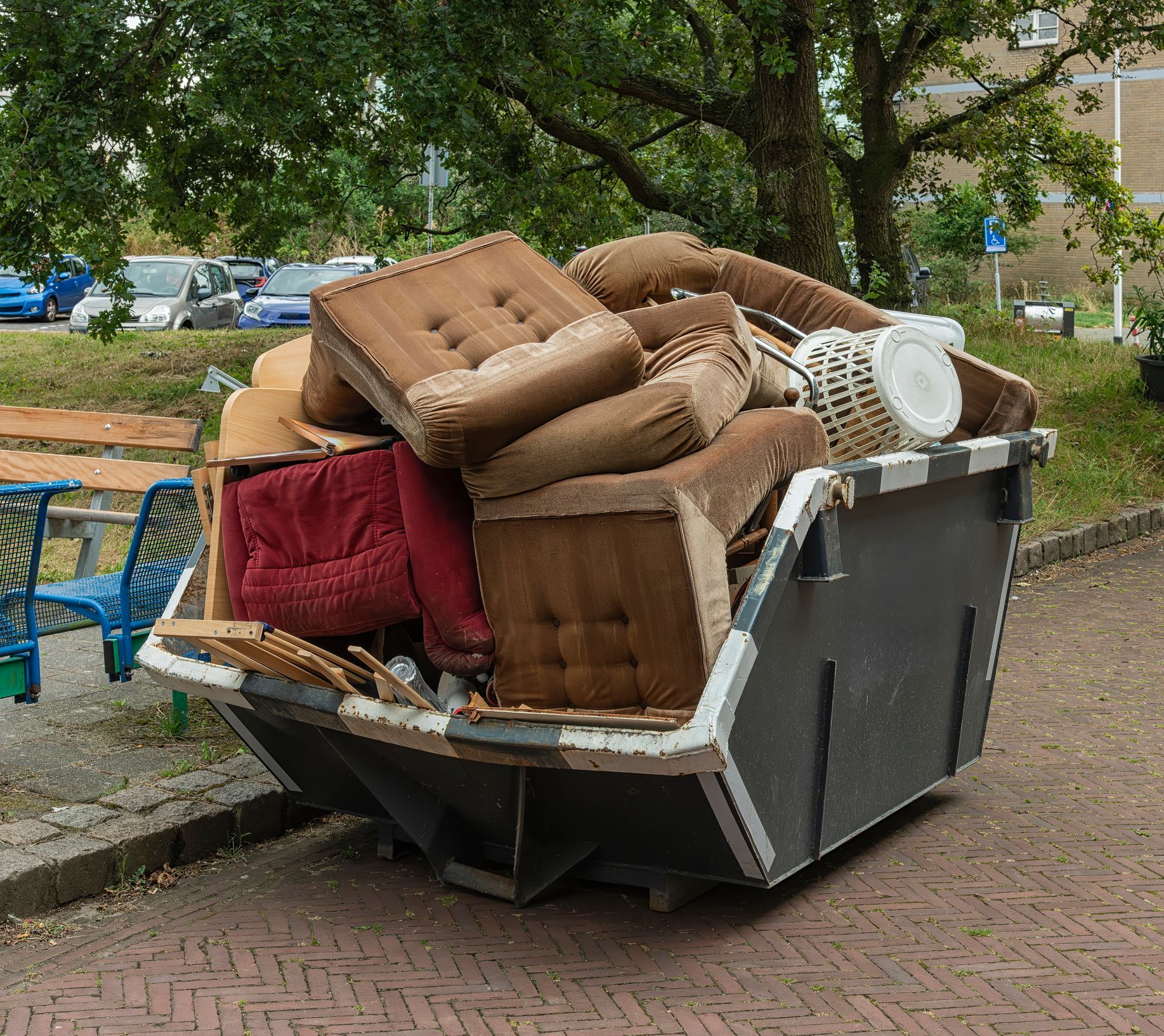 A dumpster filled with furniture is parked on the side of the road.